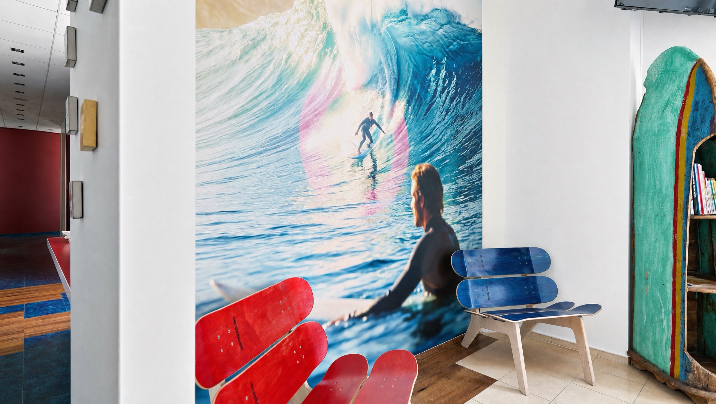 Wartebereich mit Wellen-Wandbild, Skateboard-Bänken und Surfboard-Regal